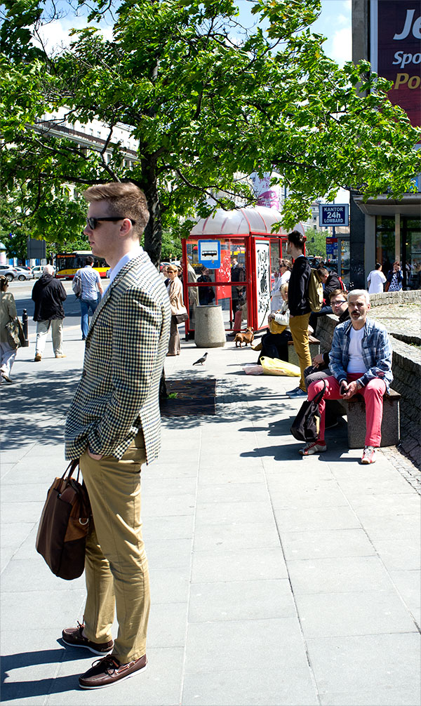 A young man dressed in H&M clothes is watched by an older man on the street in Poland