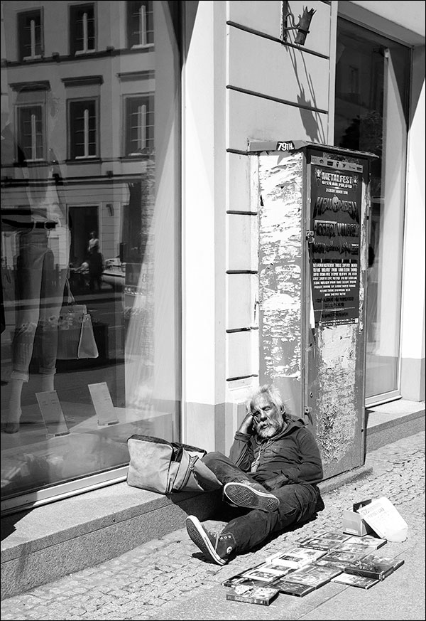 Old man asleep on the streets of Warsaw, in front of him his belongings for sale